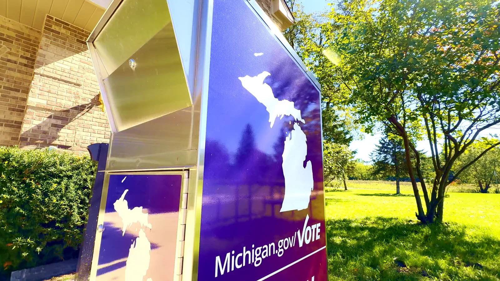 A purple official absentee ballot drop box displaying the Michigan outline in sunlight.