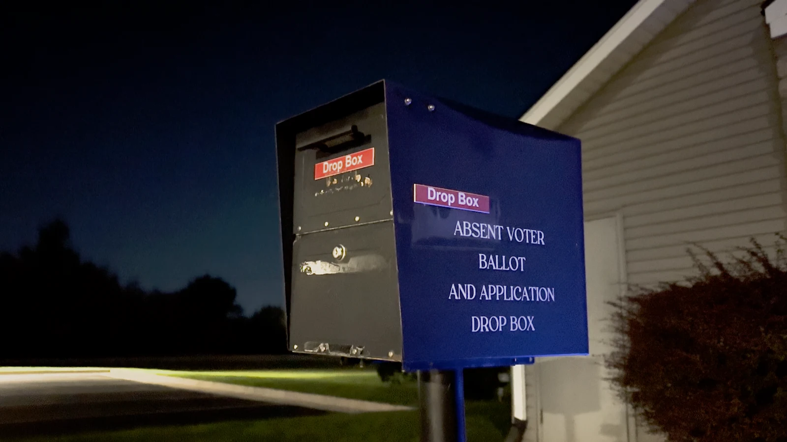 A blue absentee ballot drop box against the night sky.