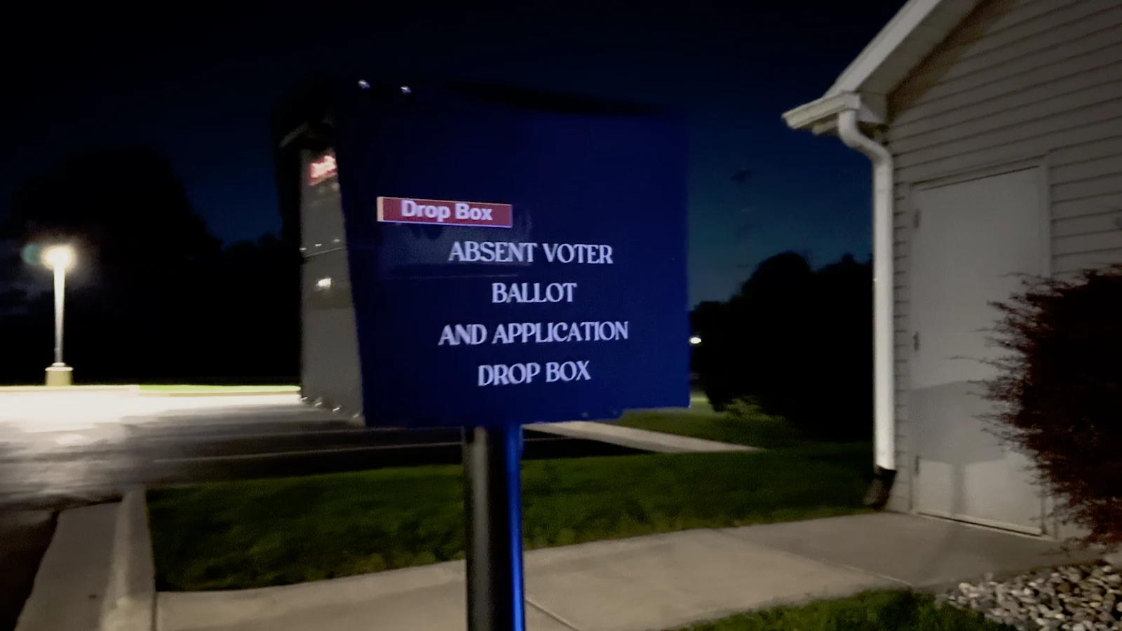 An absentee ballot drop box and its surroundings at night.