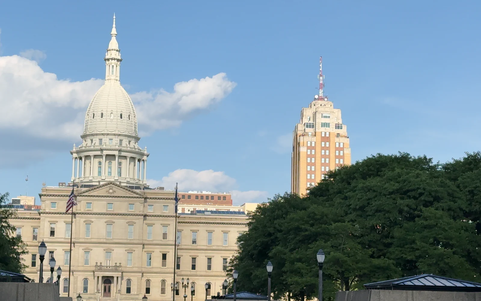 The Michigan Capitol dome and facade with trees and the surrounding Lansing skyline.