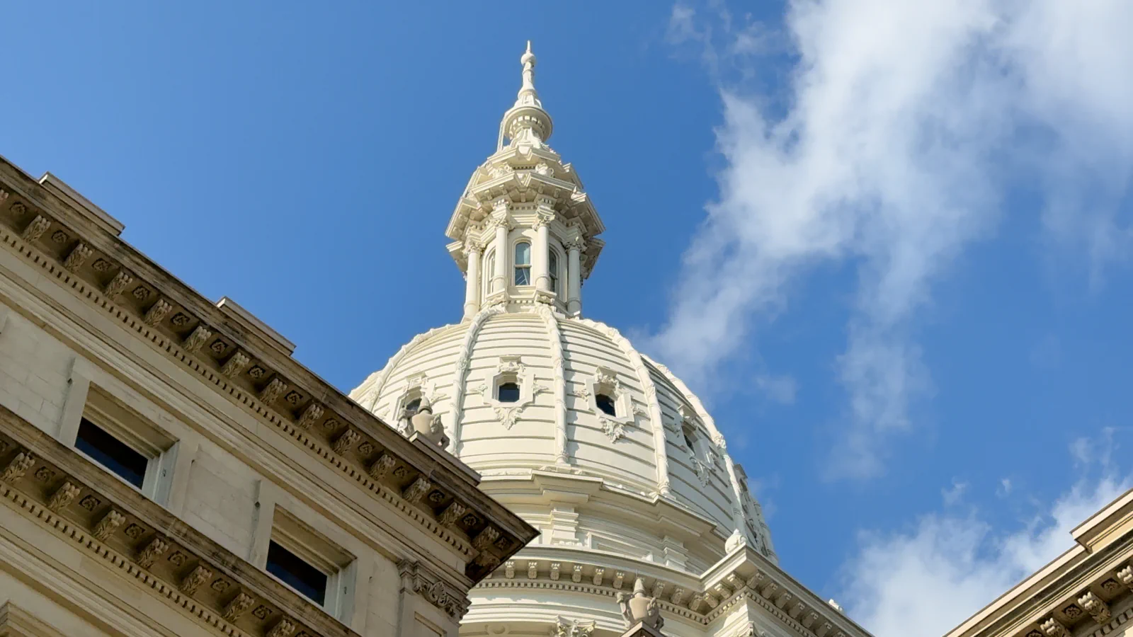The Michigan Capitol dome rising above the building cornices against a blue sky.